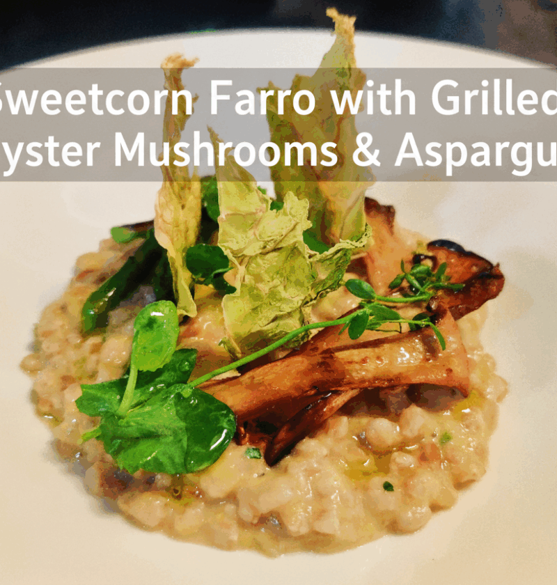 Sweetcorn Farro topped with grilled oyster mushrooms, asparagus, and pea shoots served on a white plate.