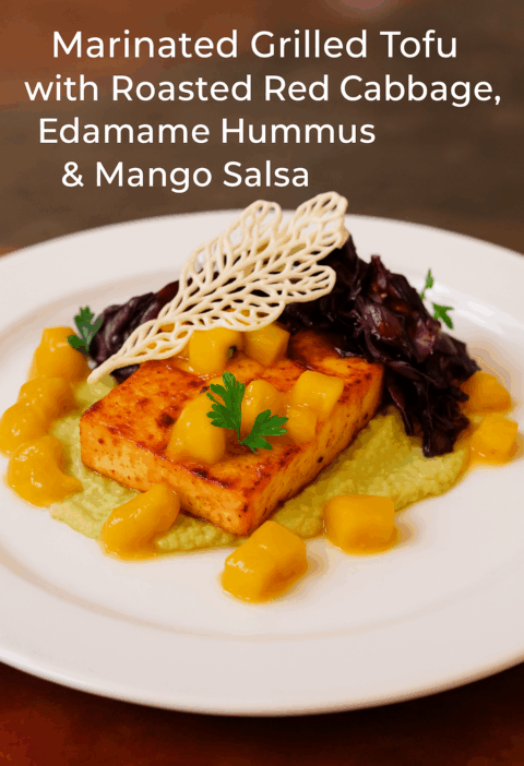 A beautifully plated vegan dish featuring marinated grilled tofu served on creamy edamame hummus, topped with roasted red cabbage, fresh mango salsa, and garnished with a crispy tuile and herbs on a white plate.