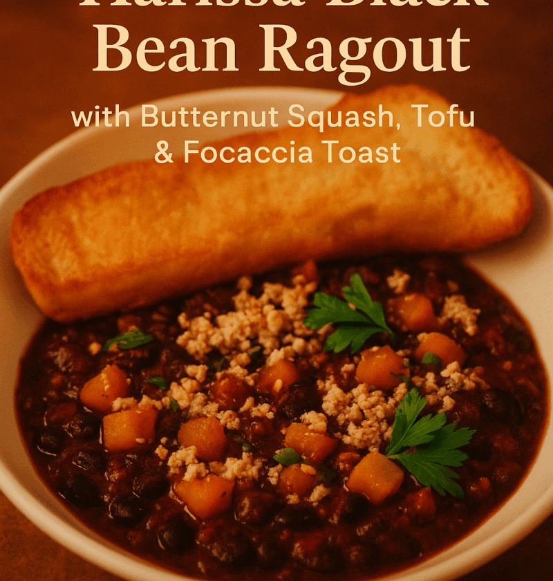 A warm bowl of Harissa Black Bean Ragout topped with roasted butternut squash, grated tofu, and fresh parsley, served with a golden focaccia slice on the side.